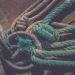 Lots of rope knots leading to moored boats. Iron mooring rings. Concrete pier surface. Nautical marine background.