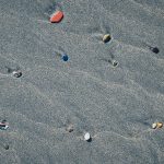 Beach beauty backdrop. Different stones with stains on the wet sand. Rare pebble background.